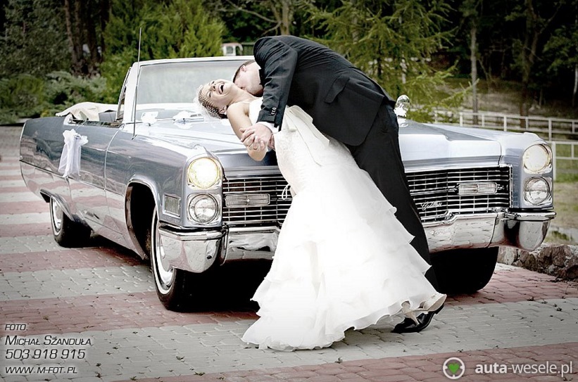 Pocałunek pary młodej na ślubnych samochodzie
